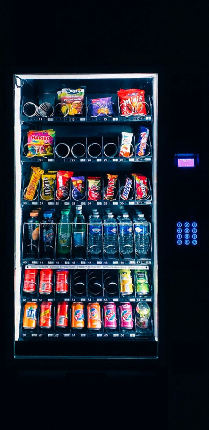 Illuminated vending machine stocked with snacks and drinks against a dark background.