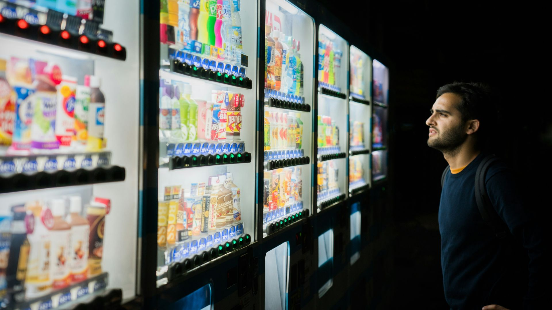 Man looking at brightly lit vending machines in a dark room