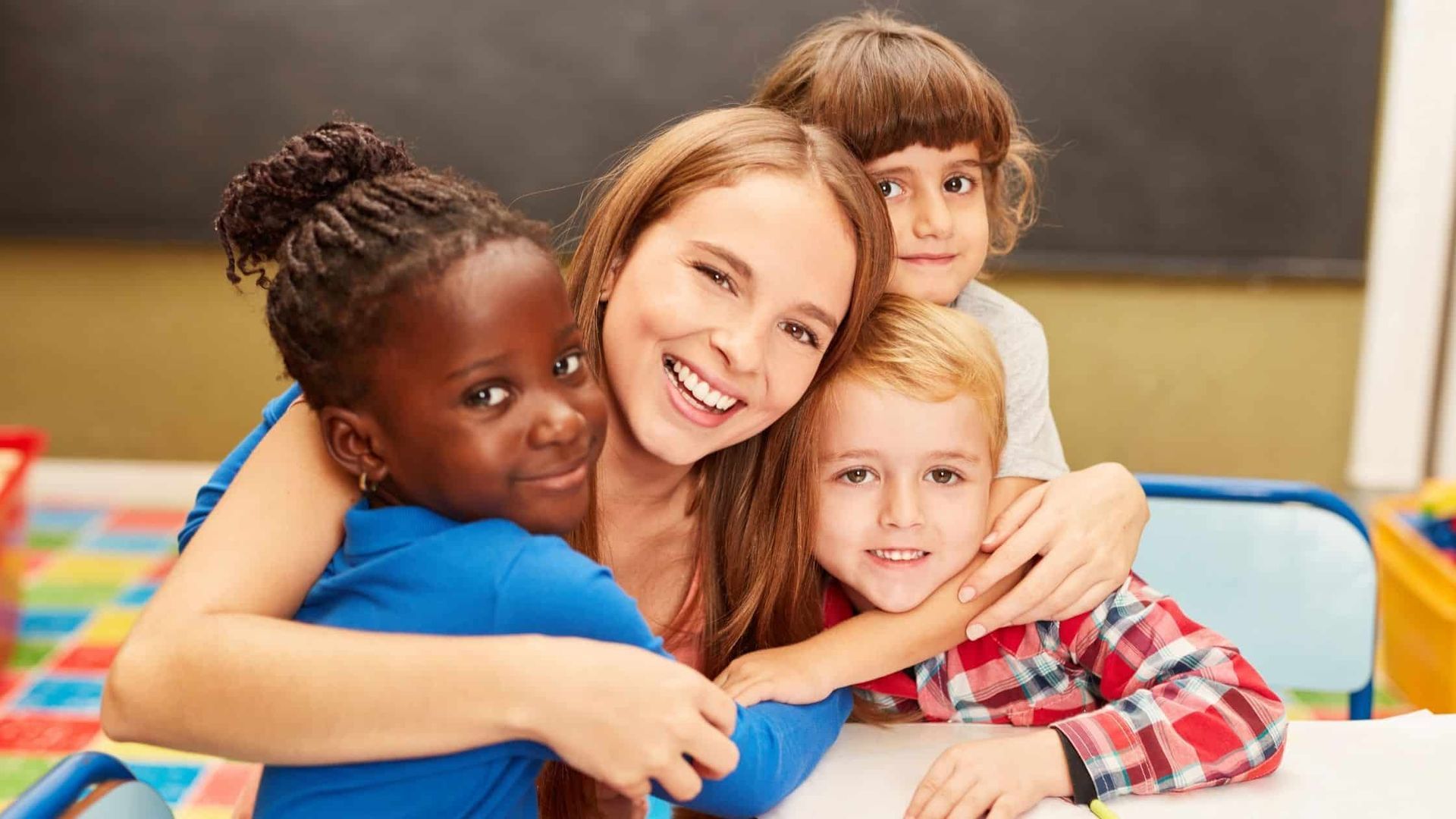 Smiling teacher hugging three children in a classroom