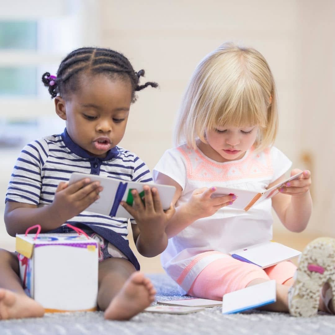 Two children sitting on a bed, reading books and opening gifts in a bright room