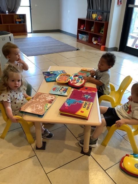 Children sitting around a low table in a playroom with books and toys.