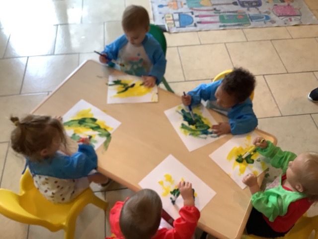Children painting at a table with colorful papers and paint in a classroom