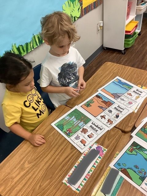 Two children read a picture book at a classroom table with colorful learning materials.
