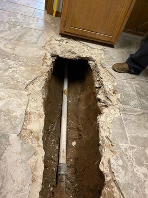 Open trench in tiled floor with exposed white plumbing pipe.