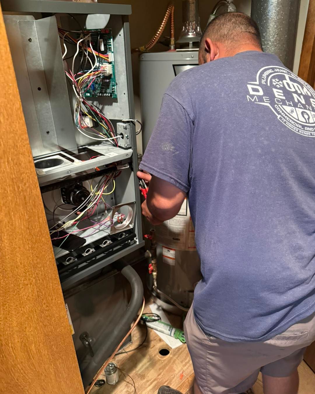 White water heater and related plumbing in a utility room. Copper and white pipes against light gray walls.