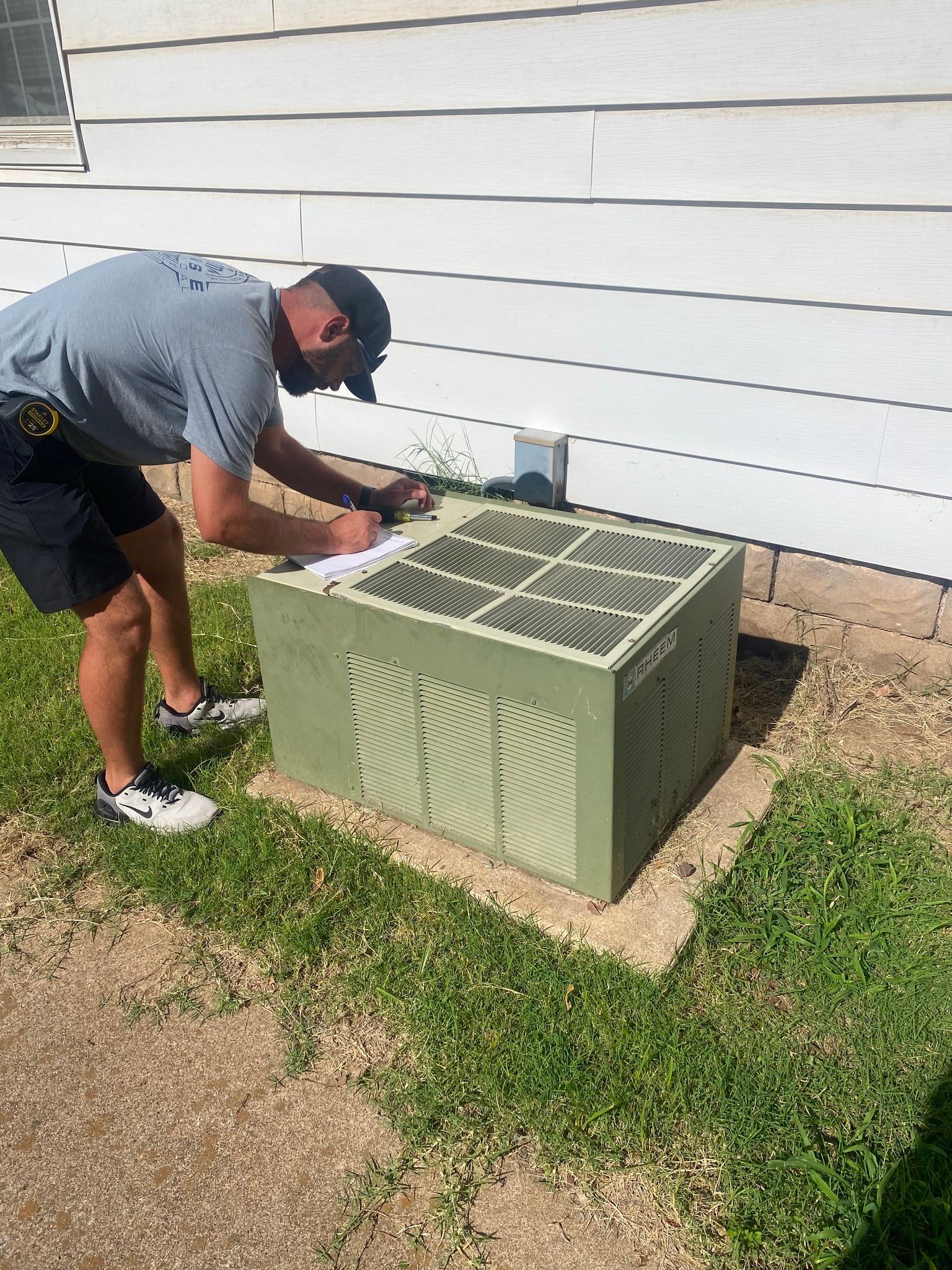 HVAC technician inspecting an outdoor unit with a multimeter.