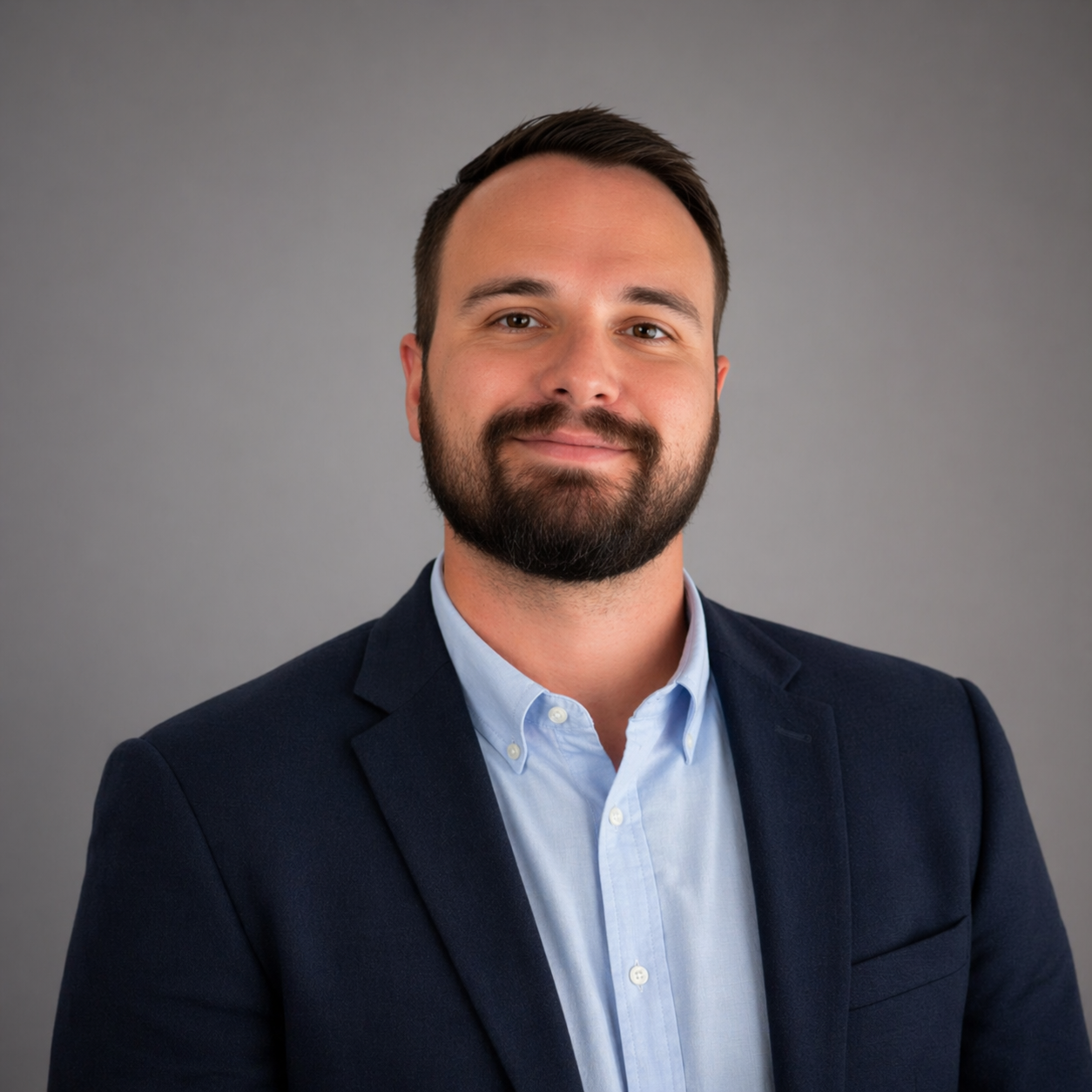Portrait of a man in a navy blazer and light blue shirt against a gray background