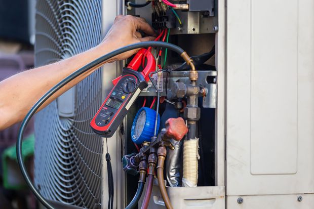 HVAC technician using multimeter and gauges to inspect air conditioning unit.