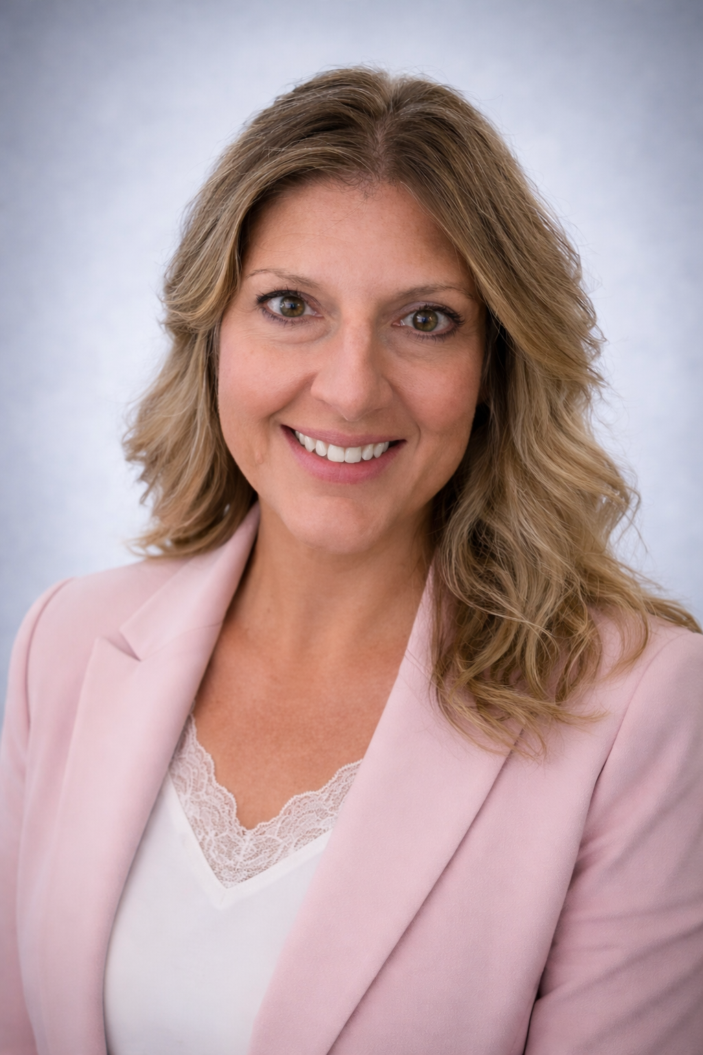 Smiling woman in a light pink blazer and white top against a soft gray background