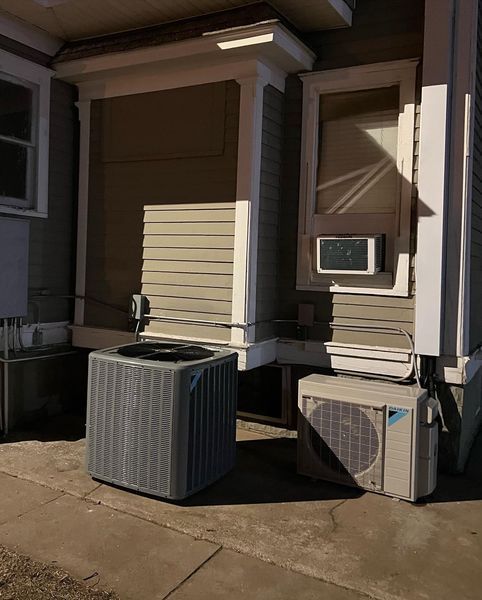 Two AC units outside a building. One is a boxy, grey unit; the other is a smaller, beige unit.