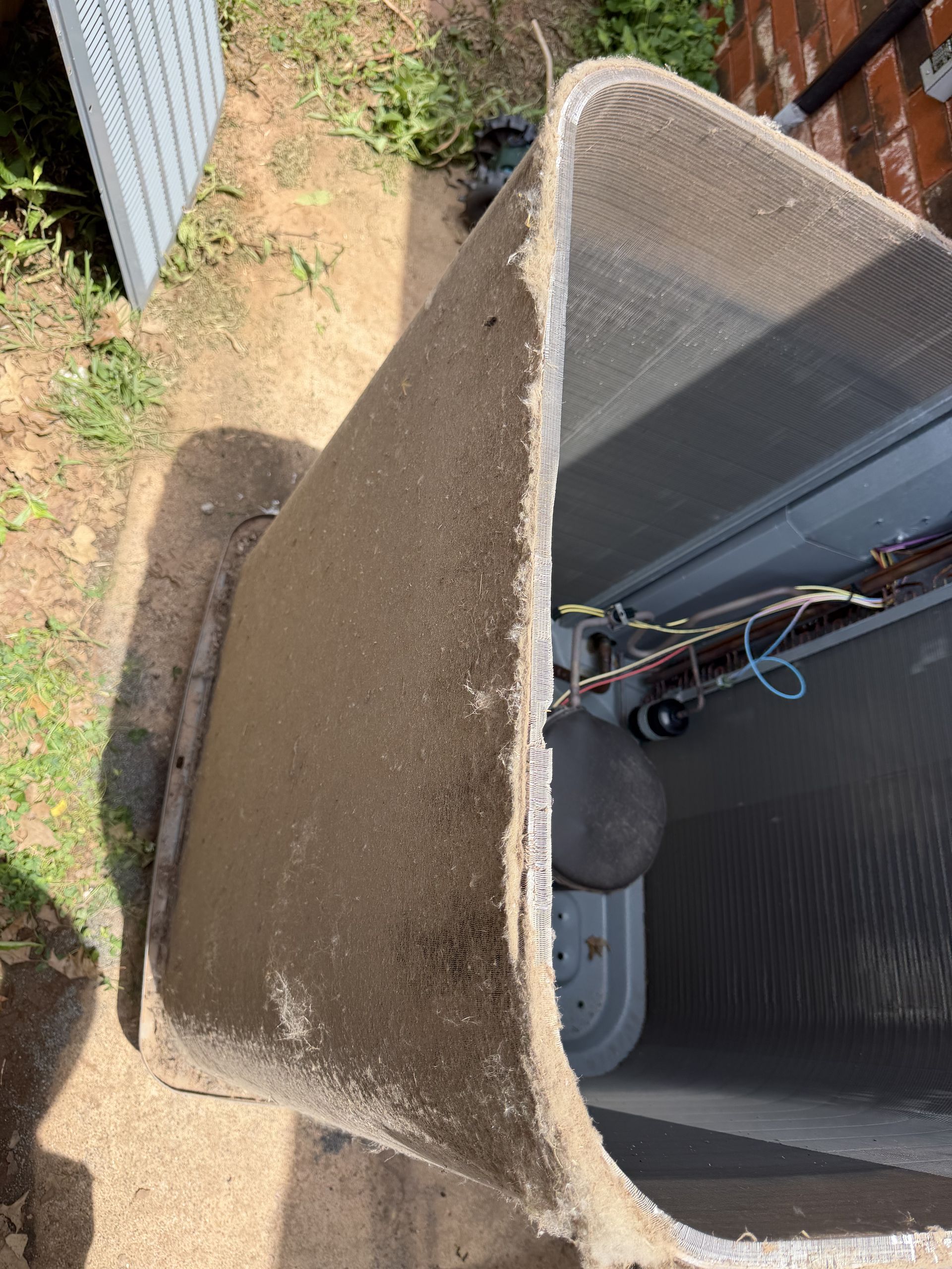 Outdoor HVAC unit with dusty beige housing beside a corrugated metal wall and dry ground