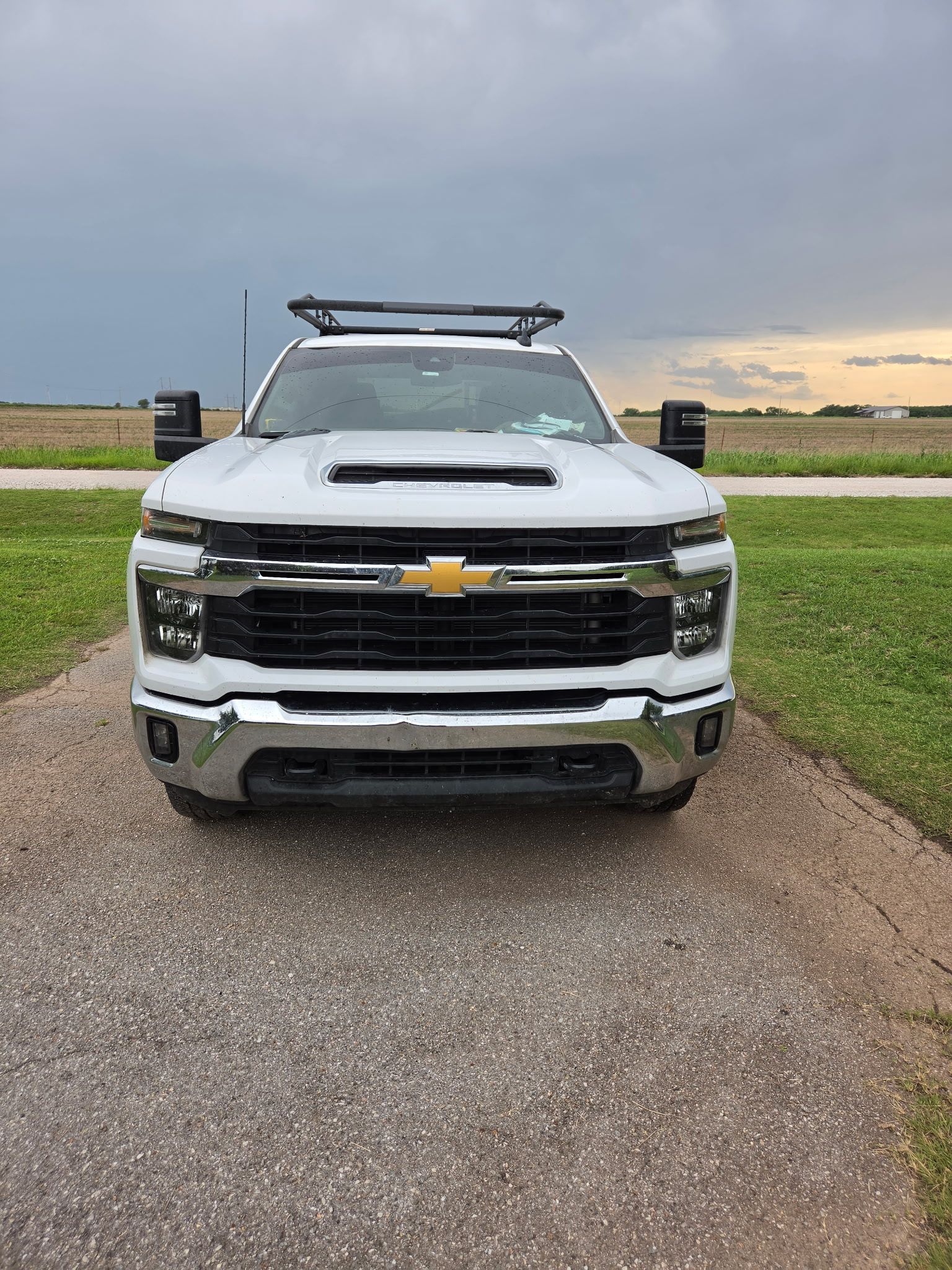 White Chevrolet pickup truck parked on a gravel road beside green fields under a cloudy sky