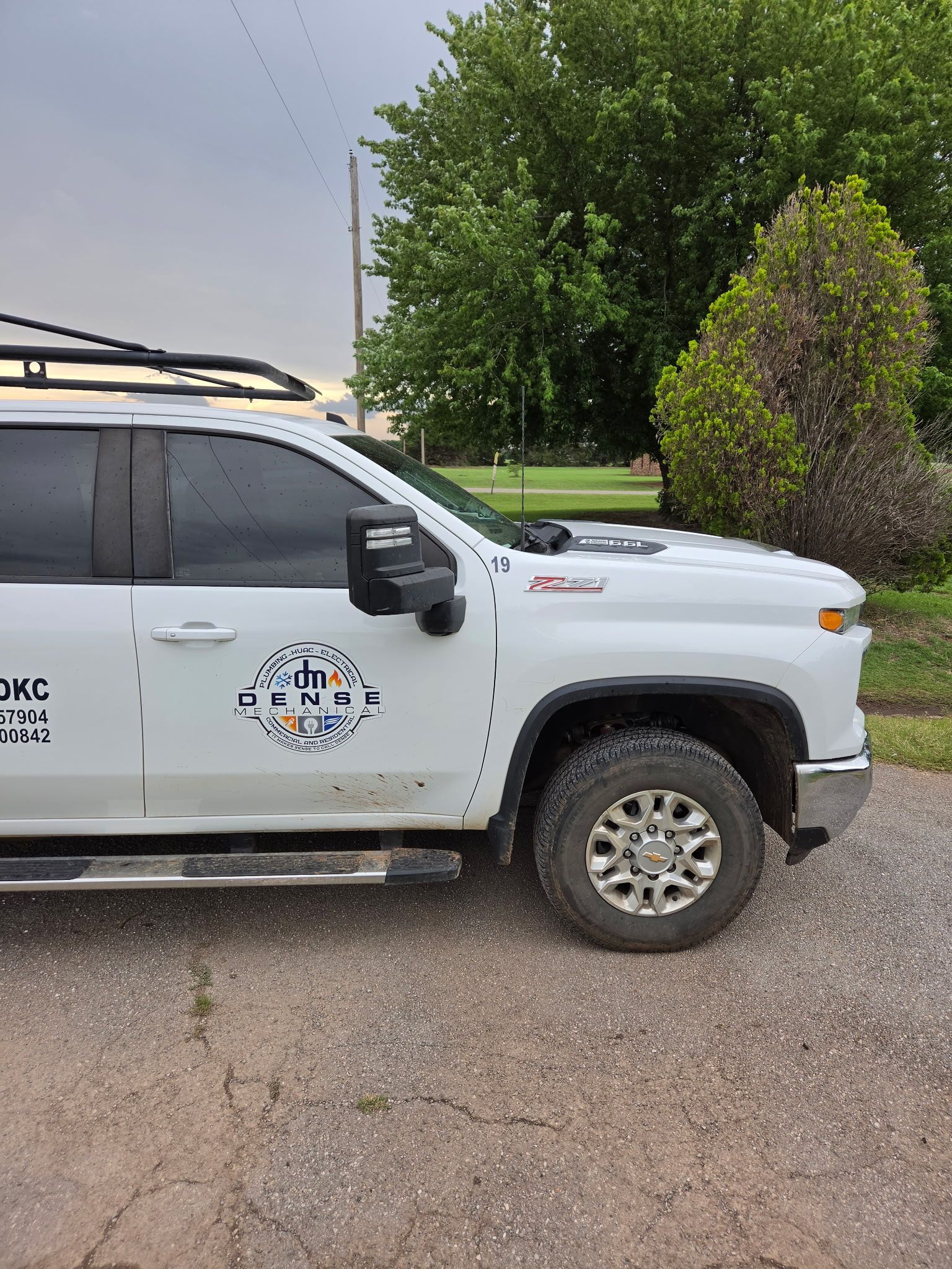 White off-road truck with roof rack parked on a gravel road beside a grassy field under a cloudy sky