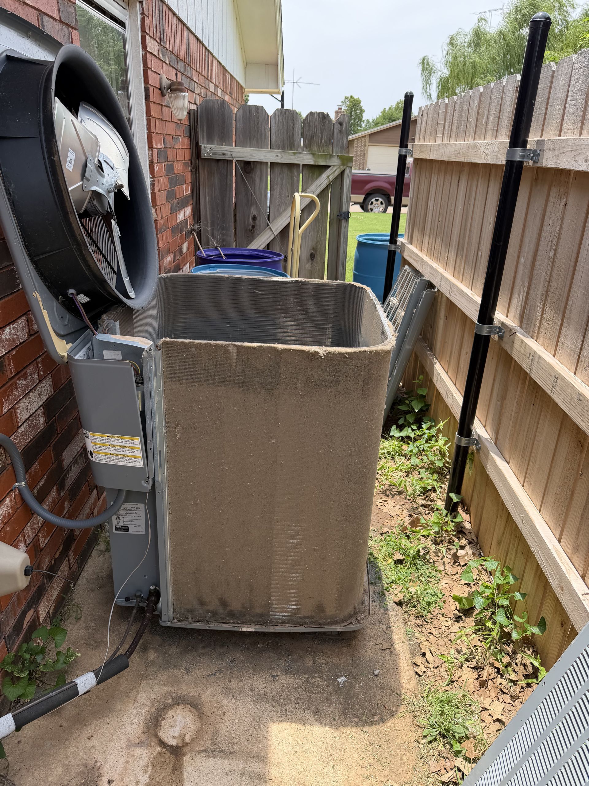 Outdoor HVAC unit beside a brick house and wooden fence in a narrow side yard.