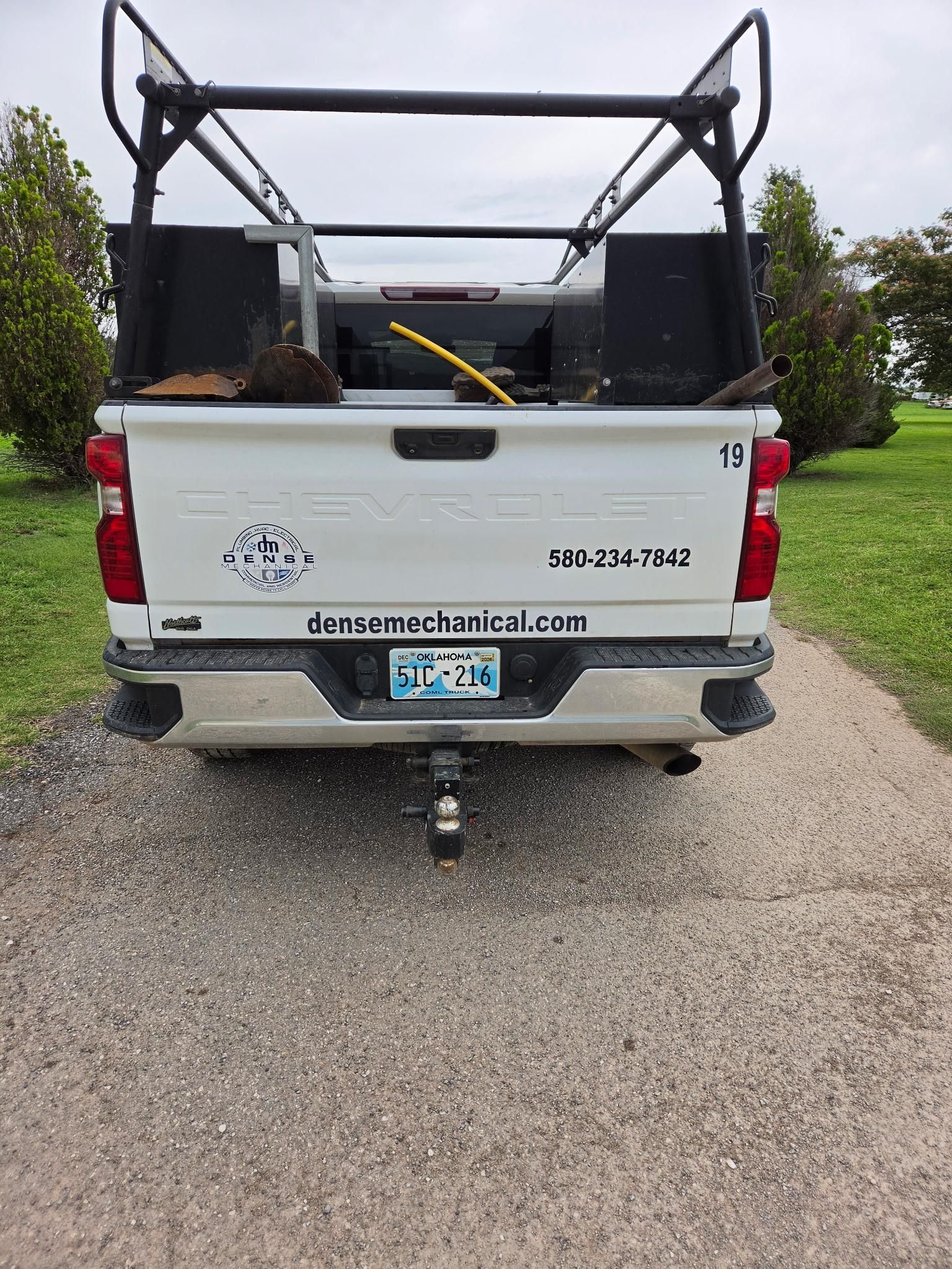 White pickup truck with a black metal cage and yellow tool in the bed, parked on gravel.