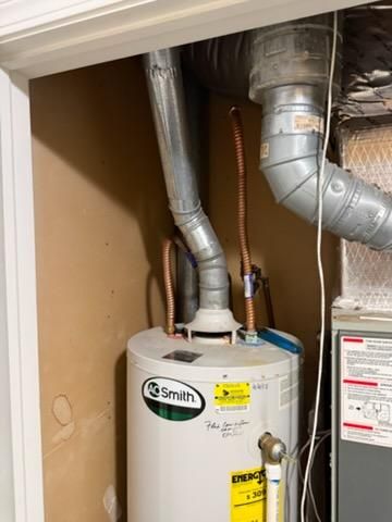 Water heater and furnace in a basement utility room, flanked by white walls and a gray floor.