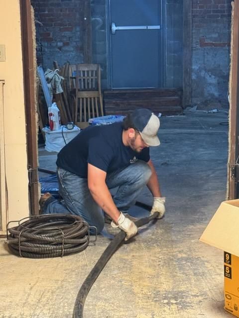 Plumber working on a toilet, tools in foreground on tile floor, bathroom setting.