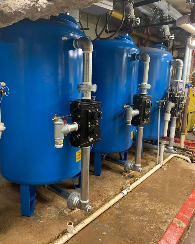 Three blue industrial water tanks with black valves and piping in a utility room.