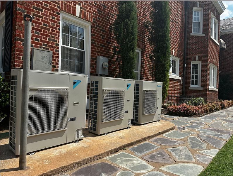 Outdoor air conditioning units lined up against a brick building on a stone path.