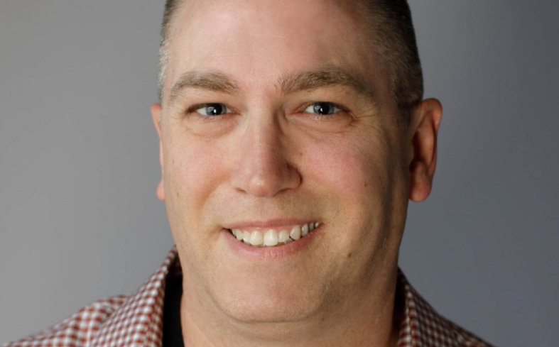 Justin Dent in a checkered shirt against a gray background