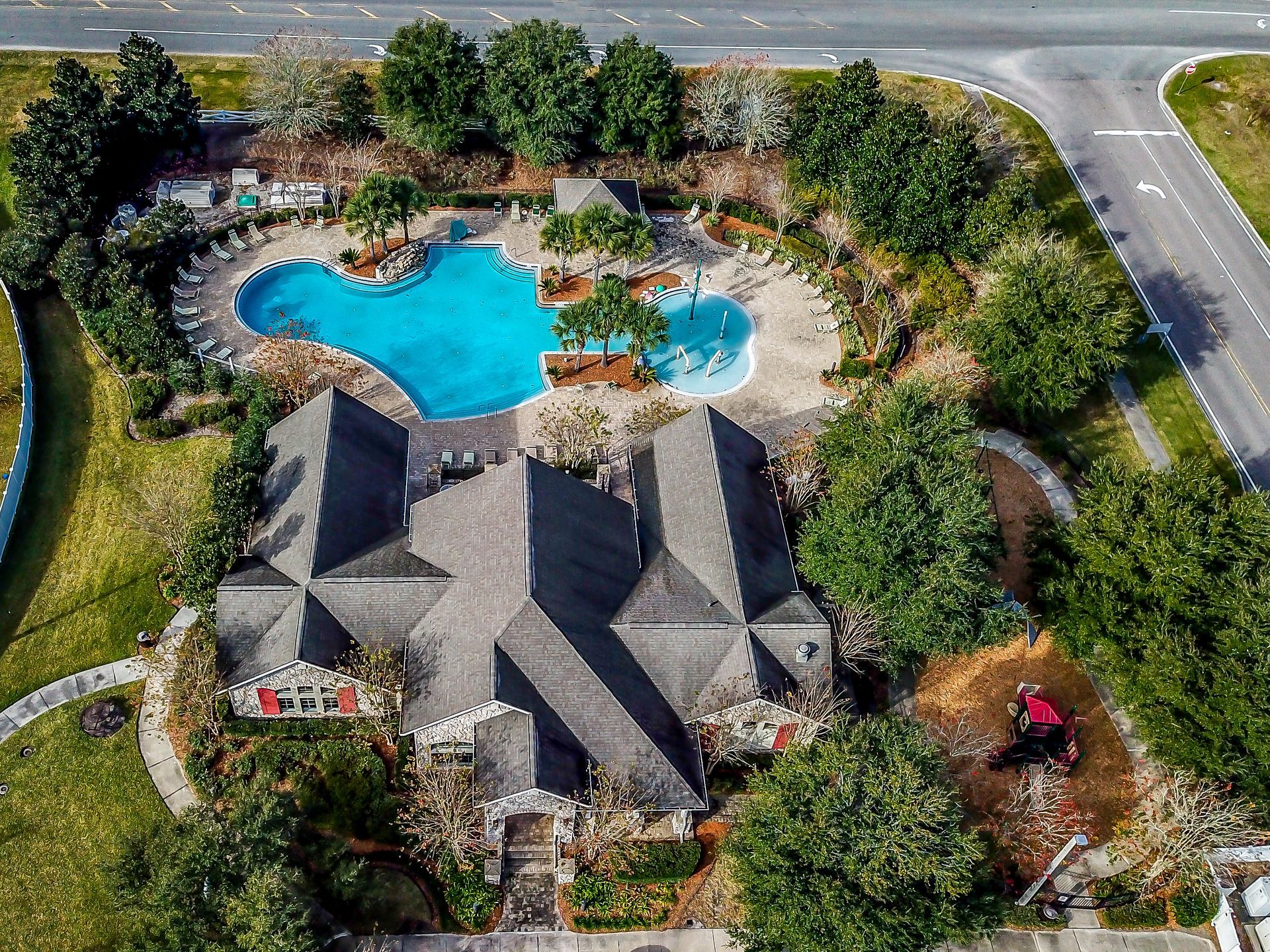 Aerial view of a house with a kidney-shaped blue pool and landscaped yard beside a road