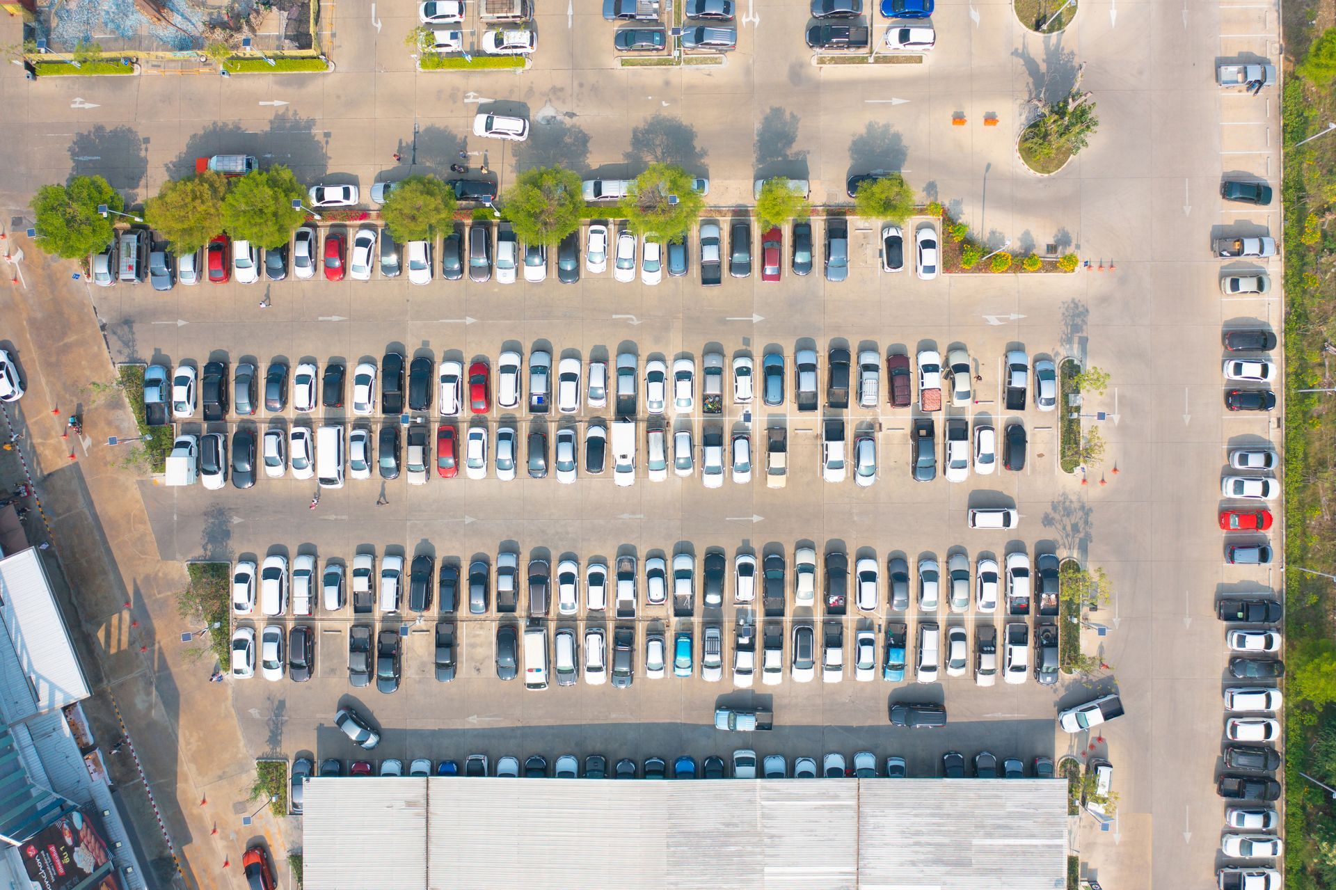Aerial view of a packed parking lot with rows of parked cars and a building edge at the bottom.