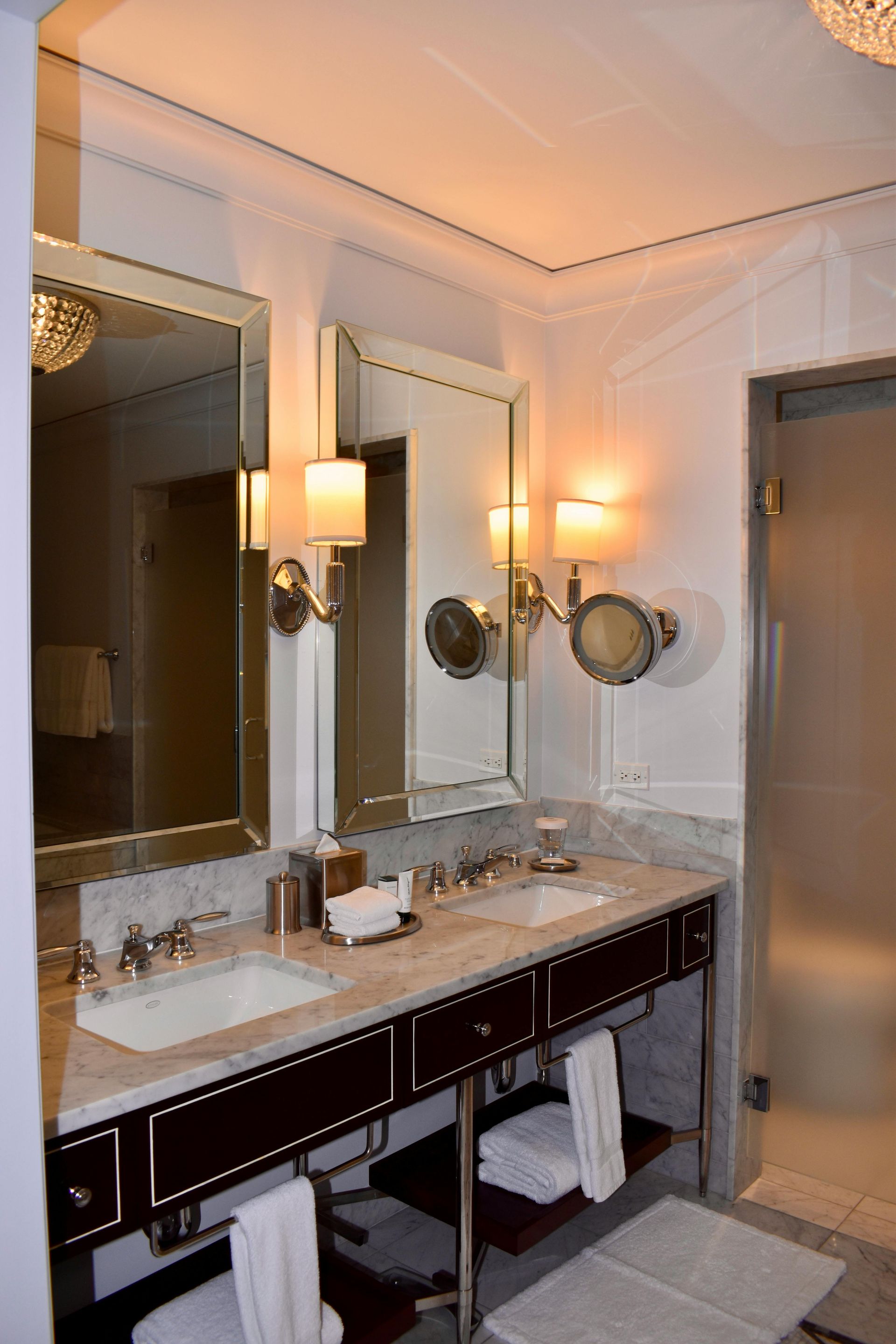 Elegant bathroom vanity with double mirrors, wall sconces, and a marble countertop beside a shower door