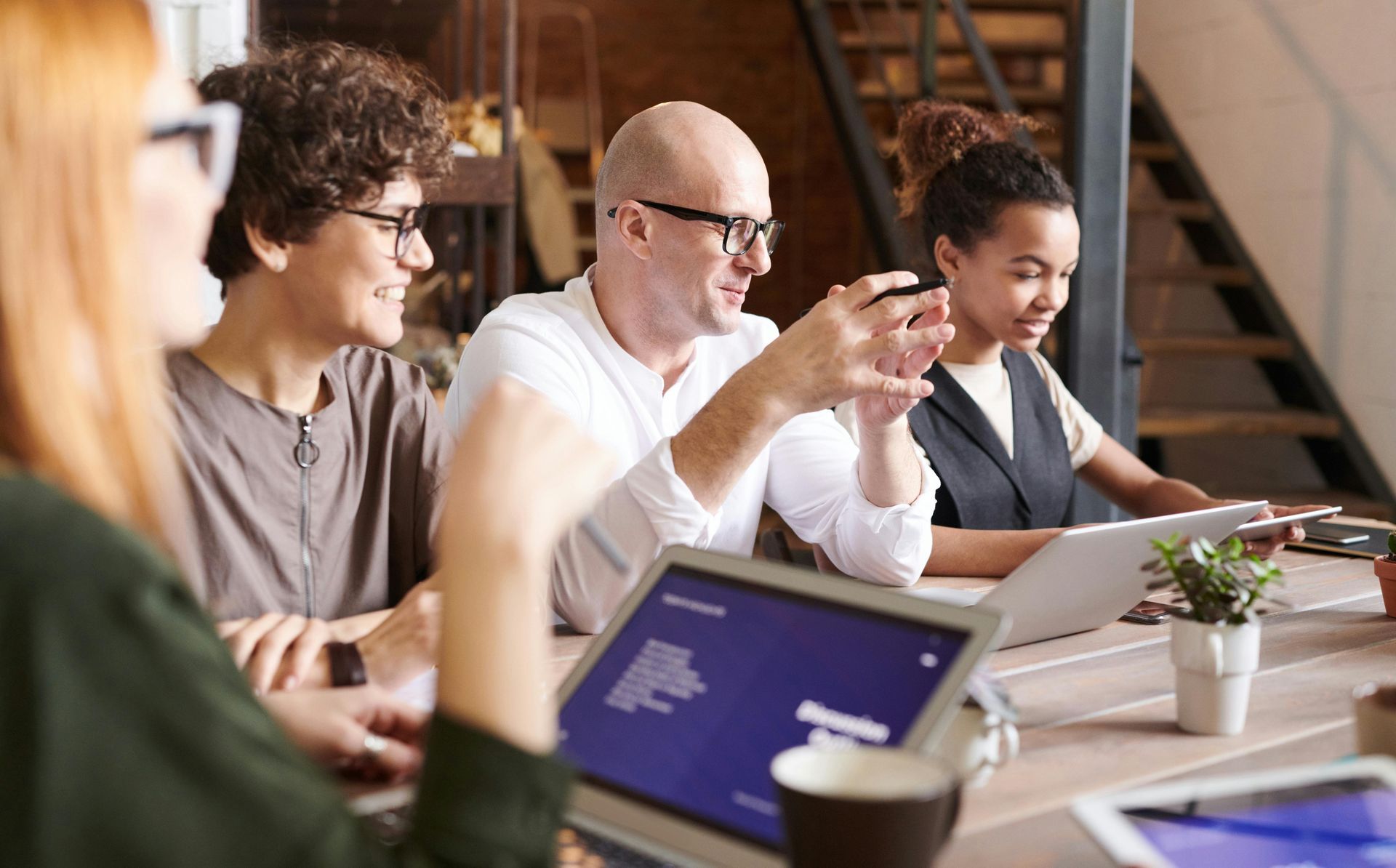 People in a meeting discussing at a table with laptops and a tablet in a bright office