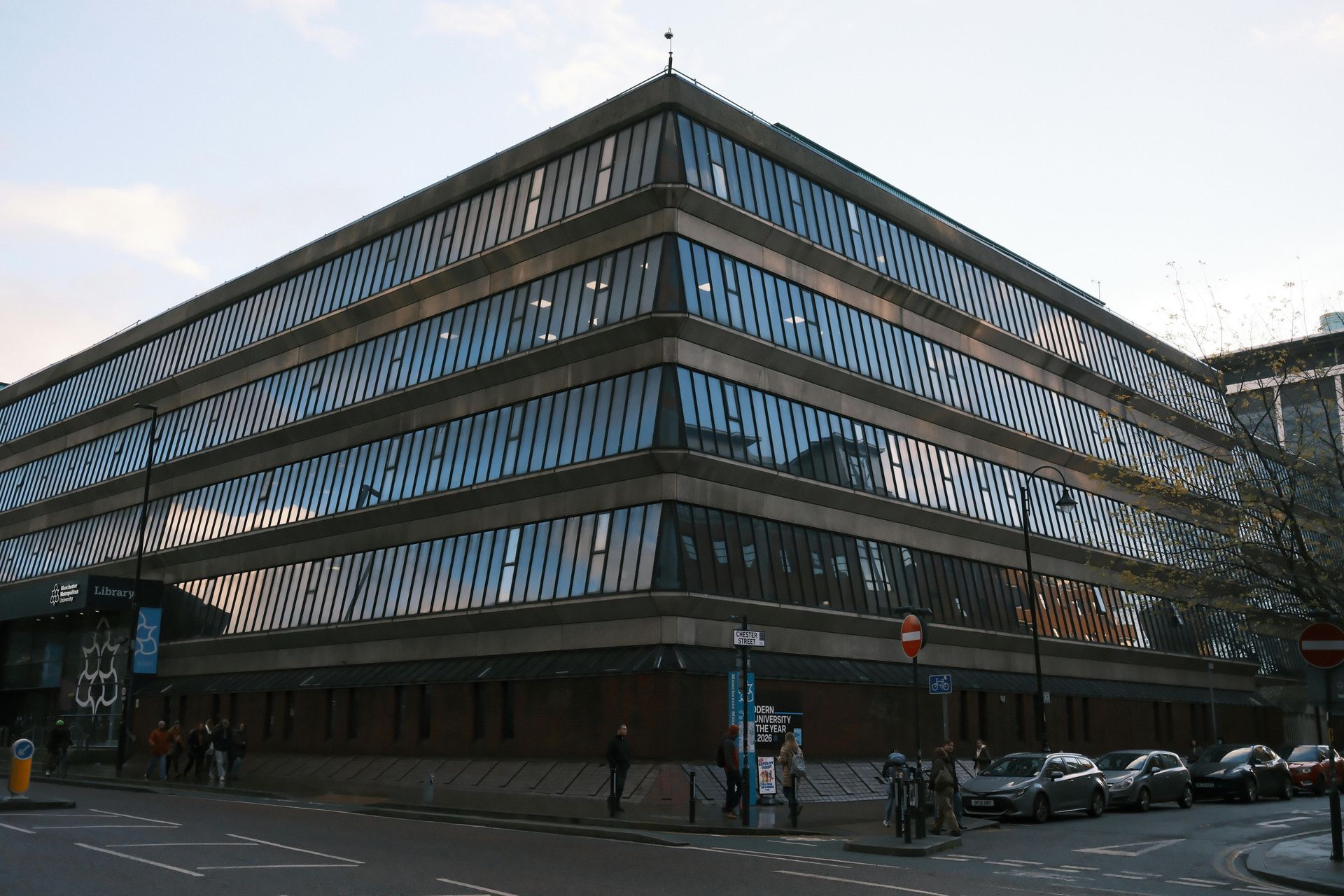 Modern multi-story office building with blue glass facade on a city street at dusk