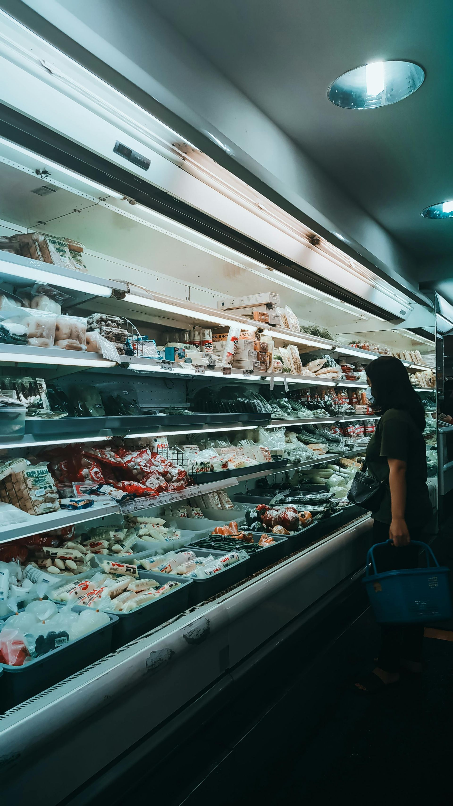 Person shopping in a brightly lit grocery store aisle beside refrigerated shelves