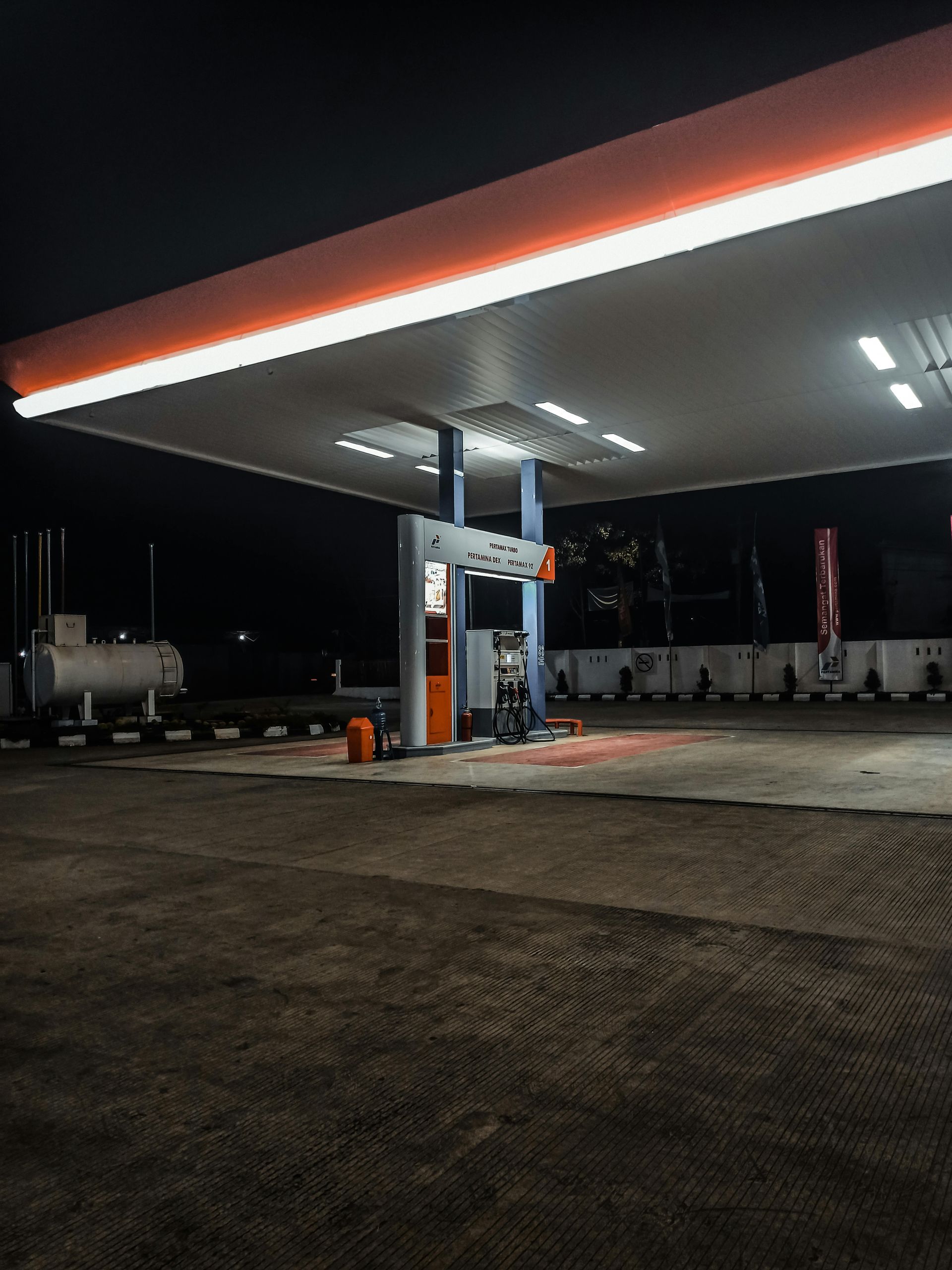 Empty gas station at night with bright canopy lights and pumps under a dark sky