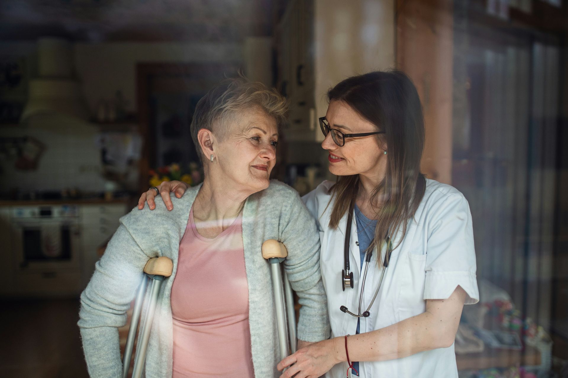 A nurse is helping an elderly woman with crutches.