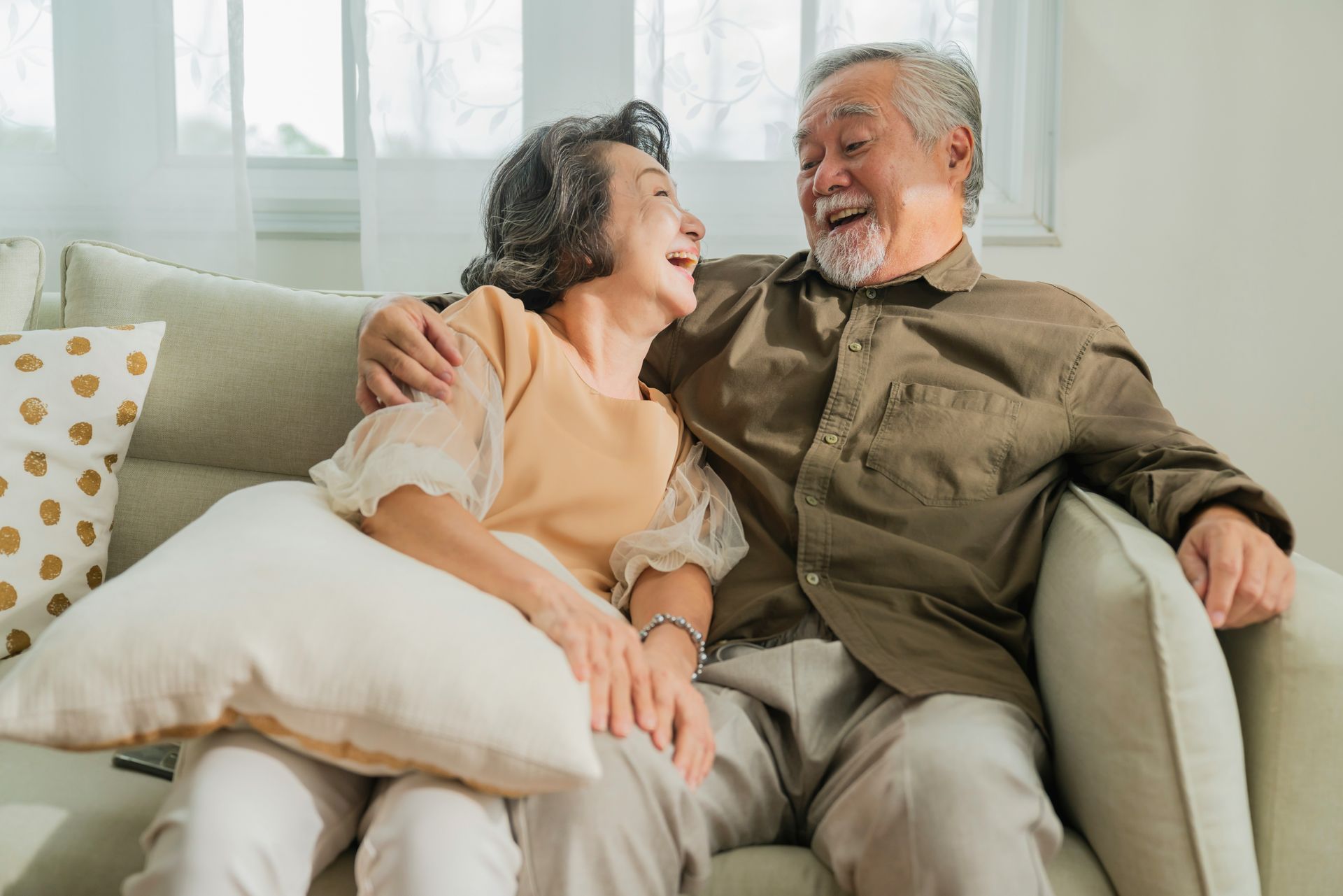 An elderly couple is sitting on a couch and hugging each other.