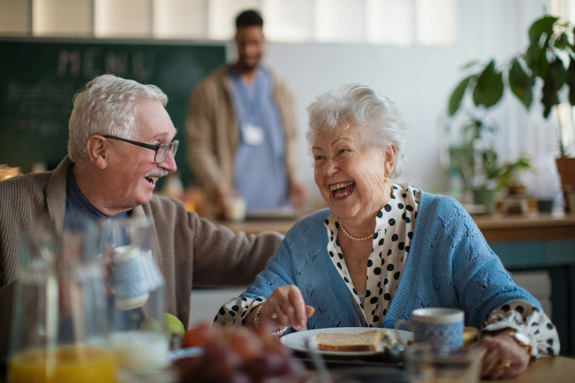 An elderly couple is laughing while sitting at a table.