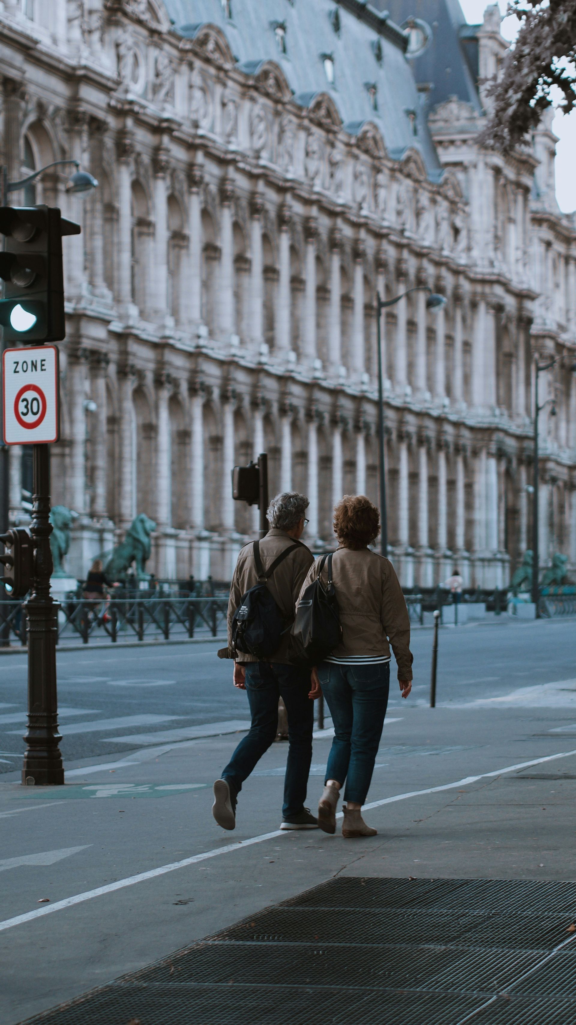 Two people are walking down a street in front of a building.