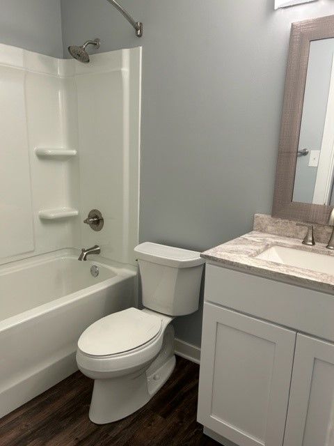 Small bathroom with white tub, toilet, and vanity on dark wood floor.