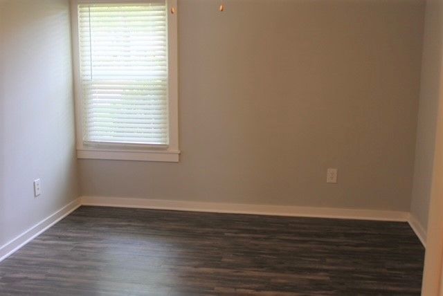 Empty beige room with dark wood floor and a single window with blinds