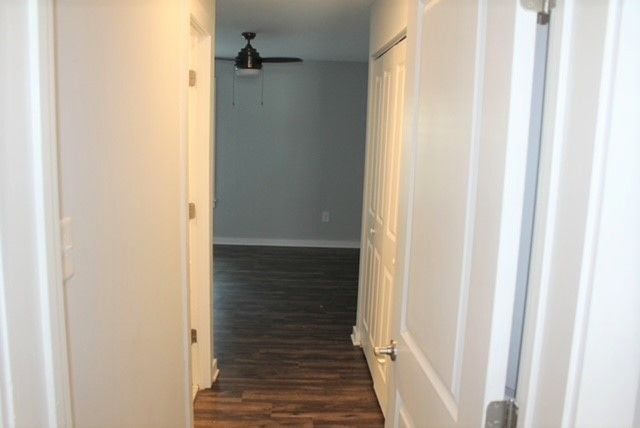 Narrow hallway with white doors, wood floor, and a ceiling fan in the room beyond.