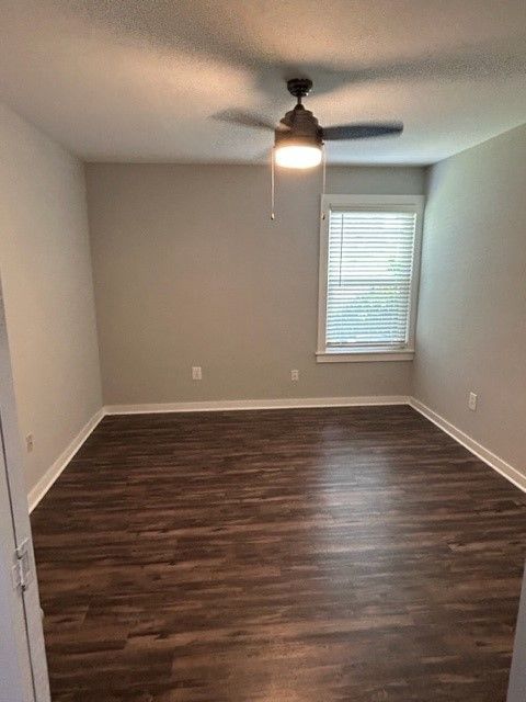 Empty bedroom with dark wood floors, gray walls, ceiling fan, and a window with blinds.