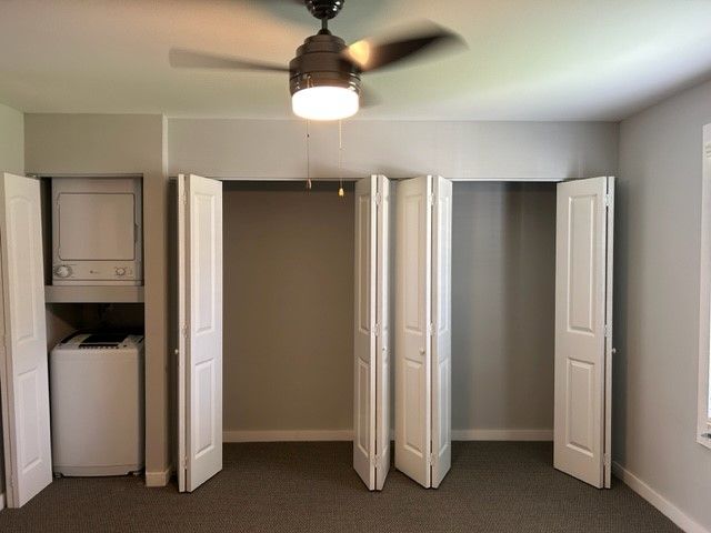Empty bedroom with open closet doors and a ceiling fan