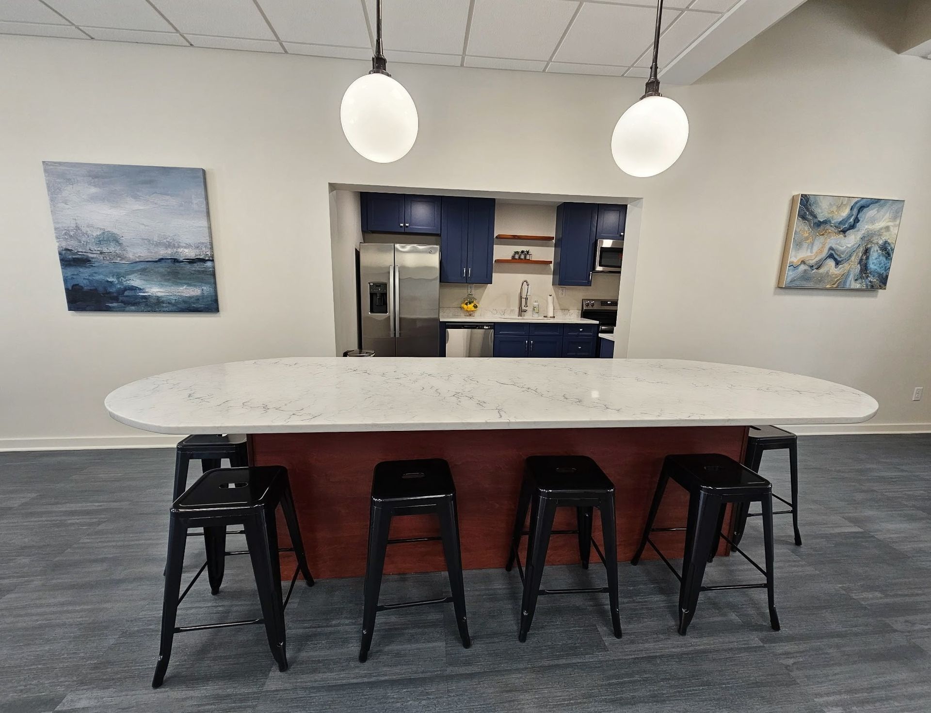 Modern kitchen with a long white island, black stools, pendant lights, and ocean-themed wall art.