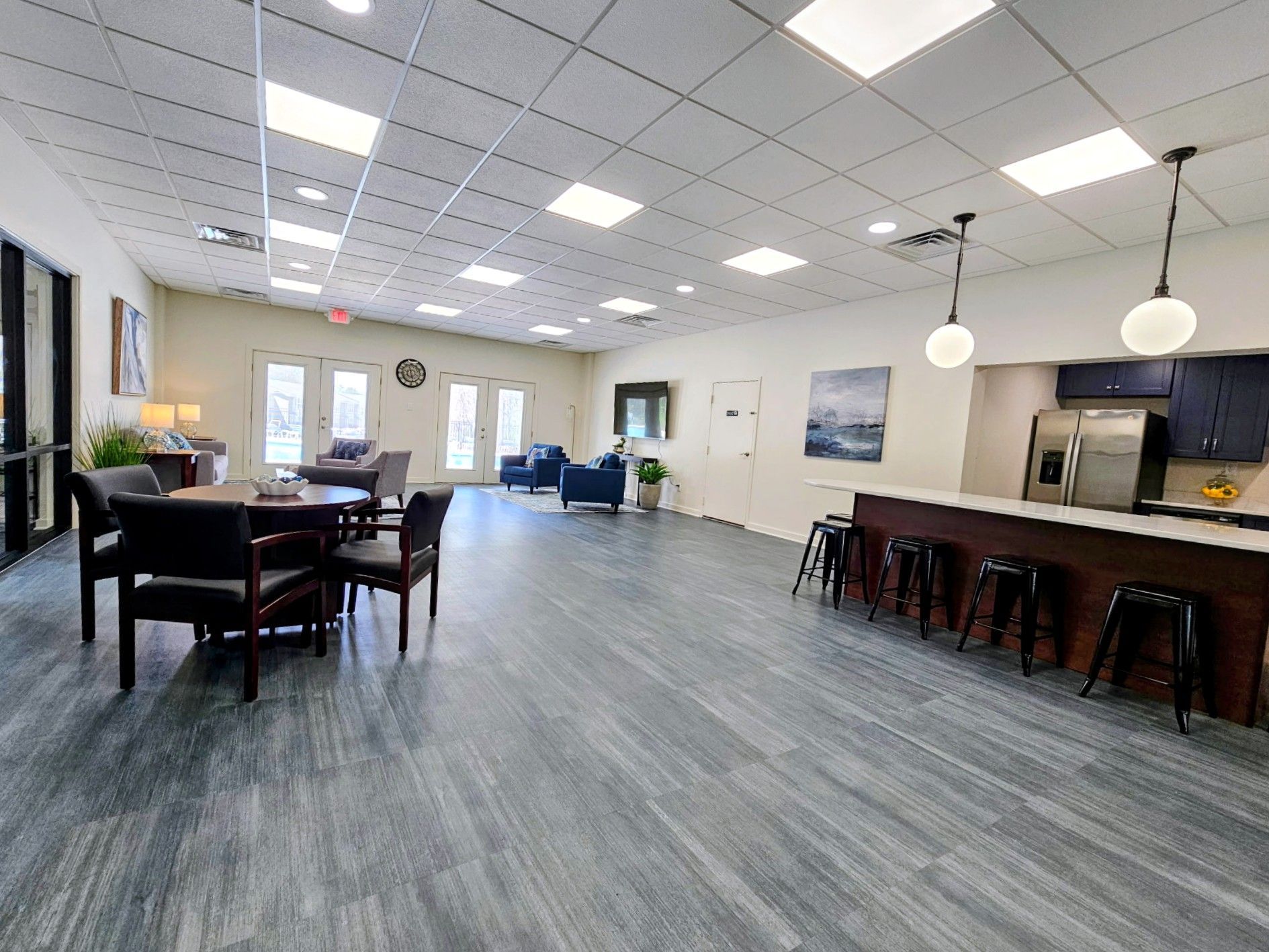 Spacious modern lounge with tables, blue chairs, bar stools, and pendant lights on a gray tile floor.