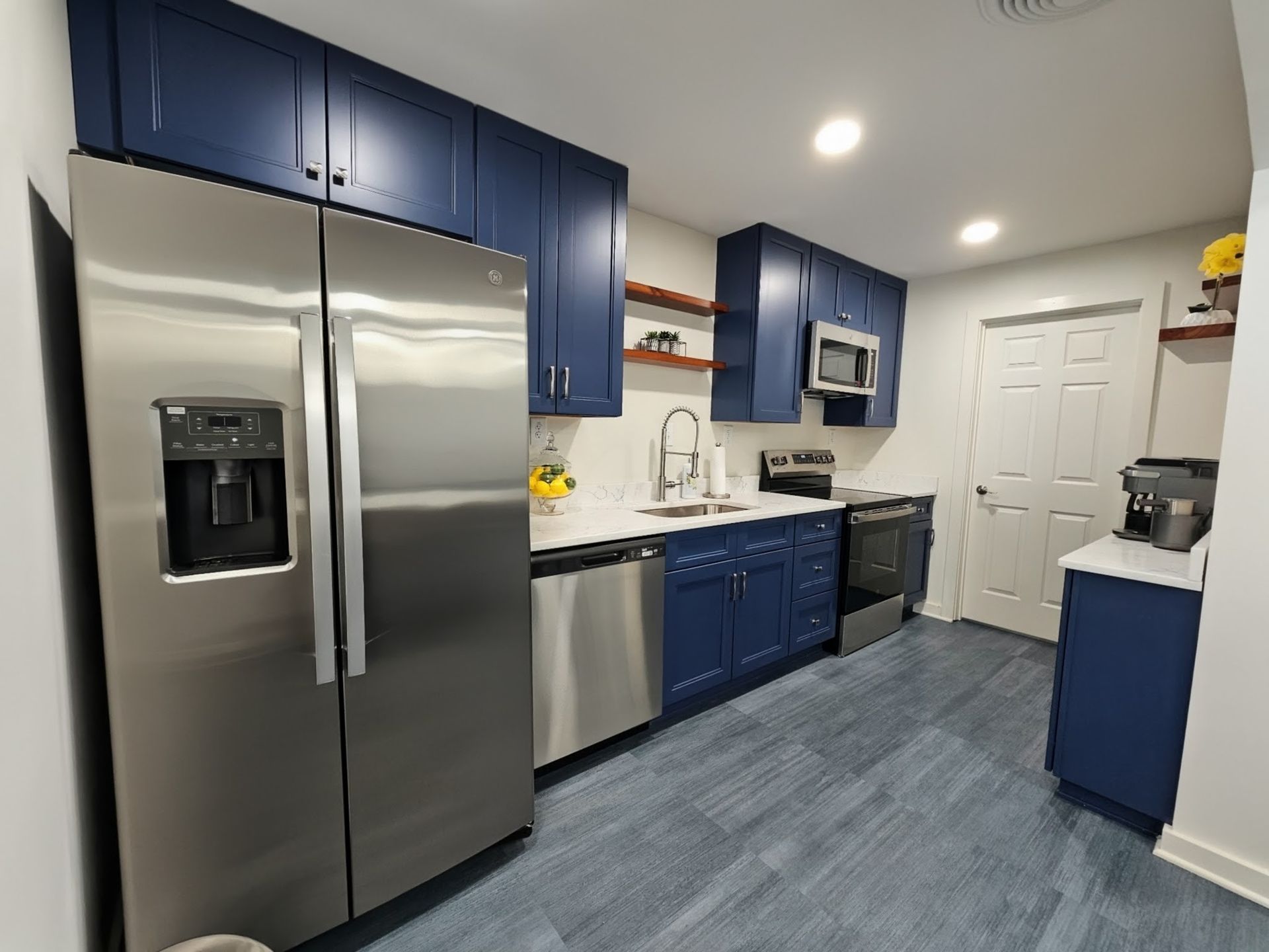 Modern kitchen with stainless steel fridge, blue cabinets, white countertops, and tiled floor