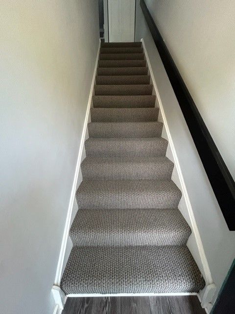 Narrow carpeted staircase with white walls and a dark handrail, viewed from the bottom up.