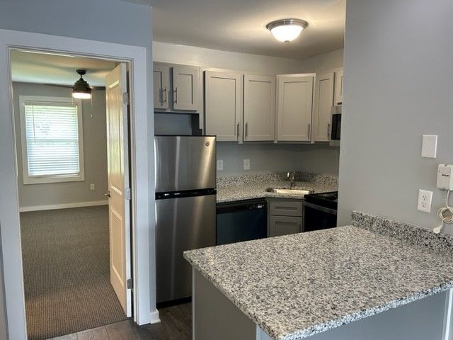 Compact kitchen with stainless steel appliances, light gray cabinets, and granite countertop opening to a carpeted room