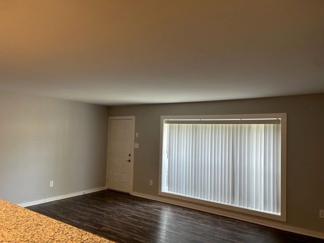 Empty living room with gray walls, dark wood floor, and large window blinds