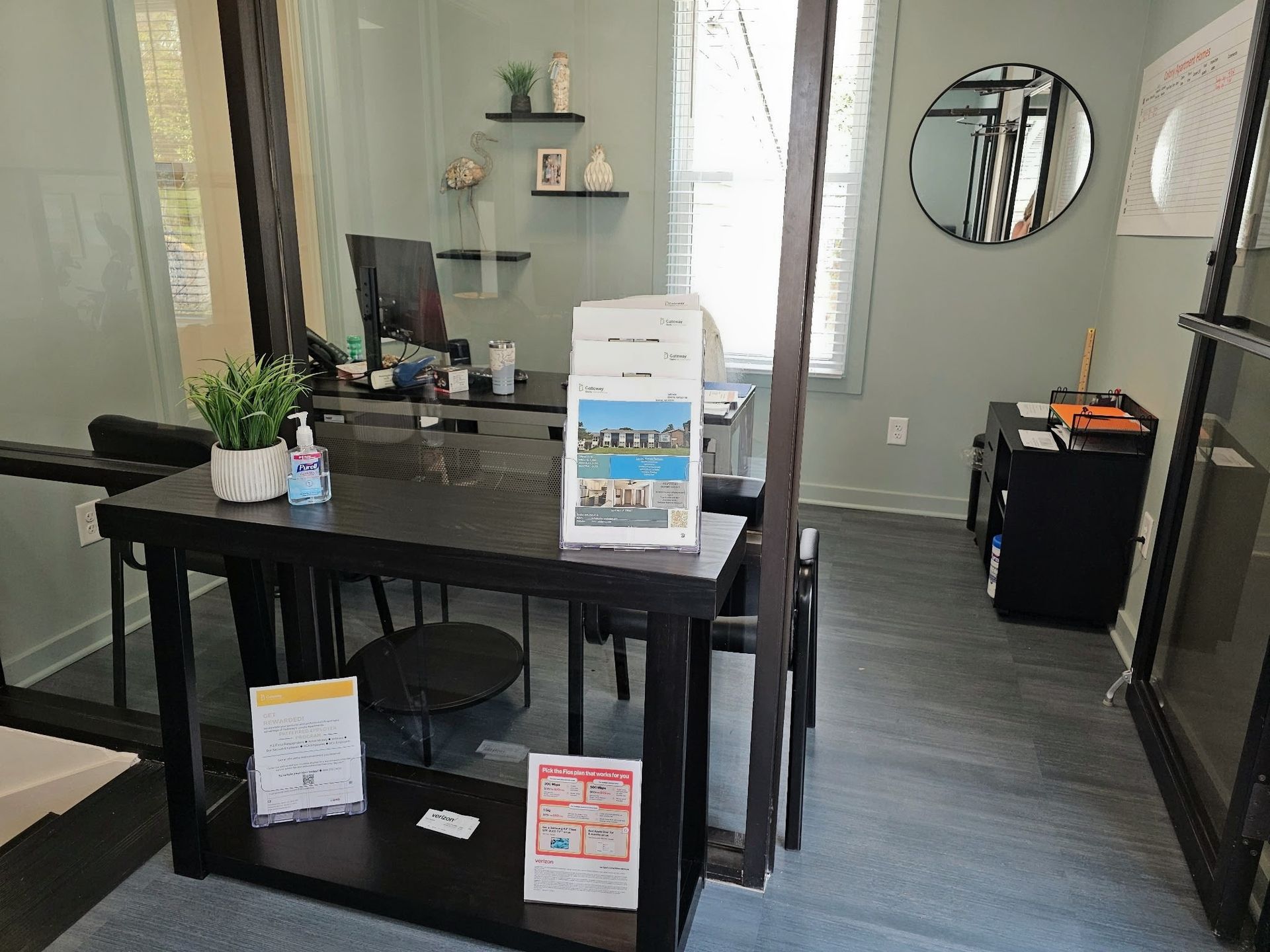 Small storefront reception area with black table, display signs, and wall shelves in a narrow hallway