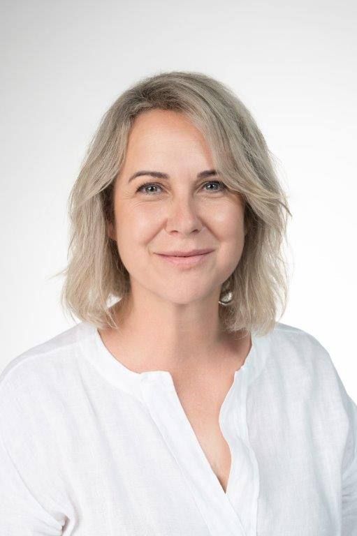 Eine Frau mit lockigem Haar trägt ein weißes Hemd und lächelt.