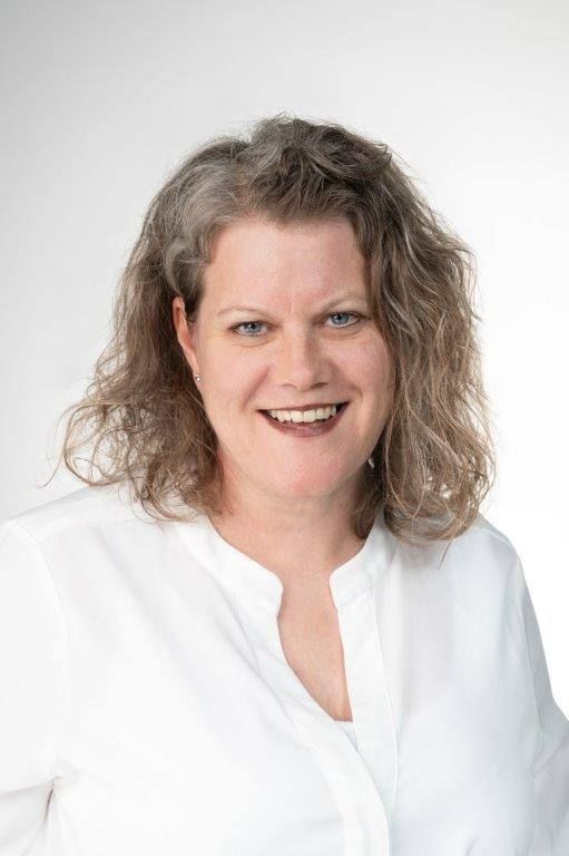 Eine Frau mit lockigem Haar trägt ein weißes Hemd und lächelt.
