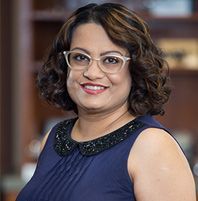 A woman wearing glasses and a blue dress is smiling for the camera.